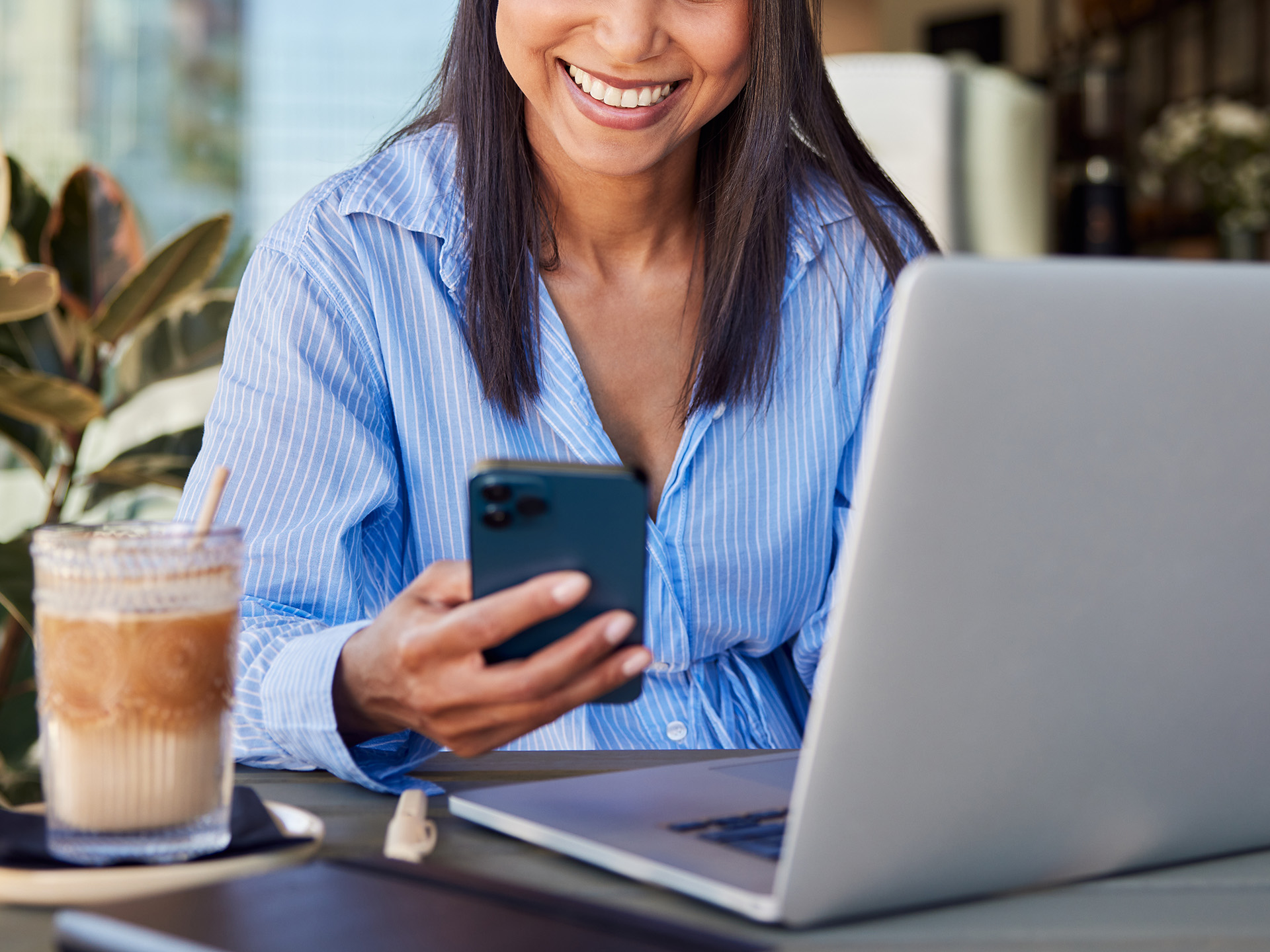 Woman using phone and laptop at cafe