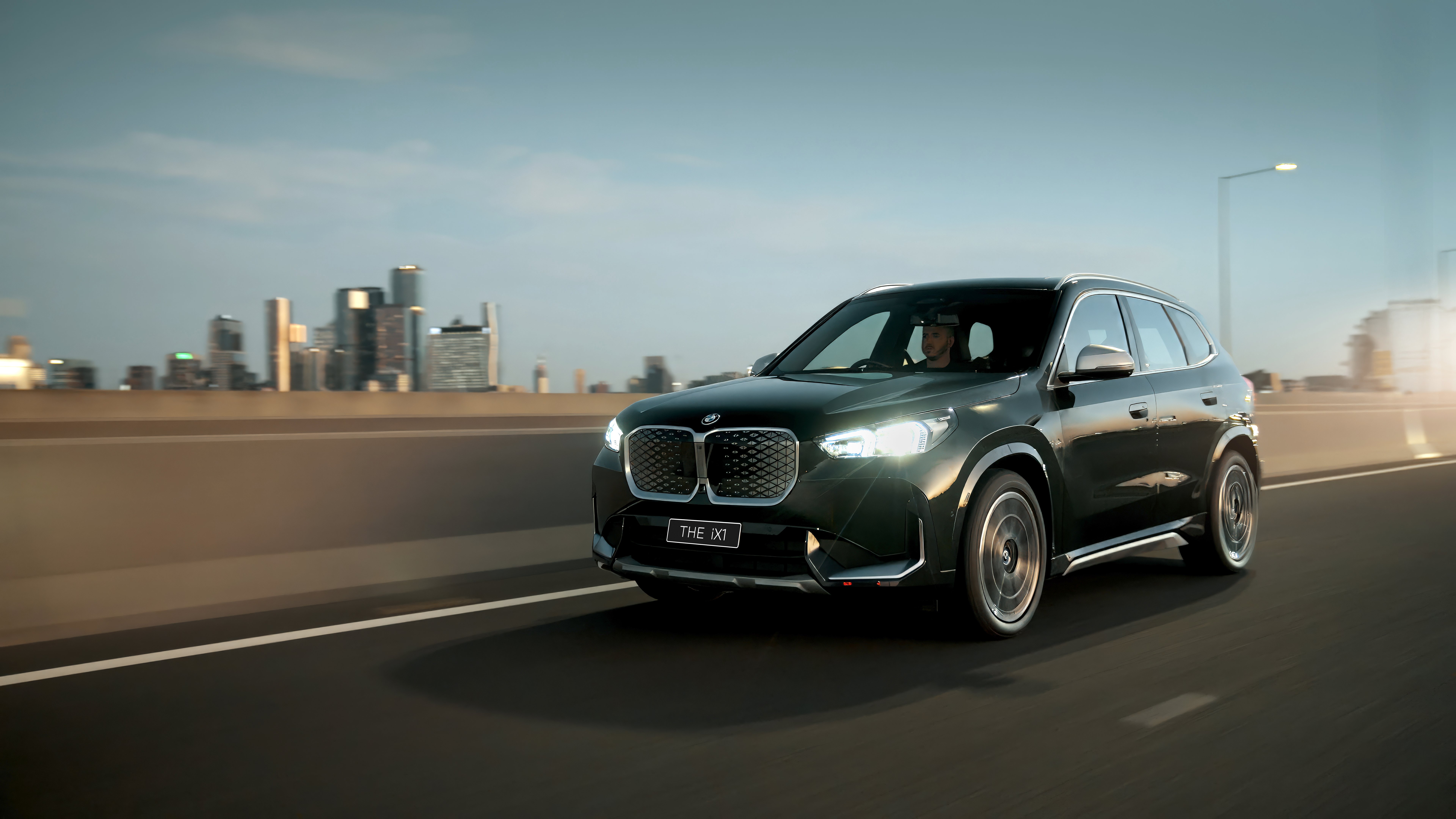 BMW X1 SUV driving past city skyline at dusk
