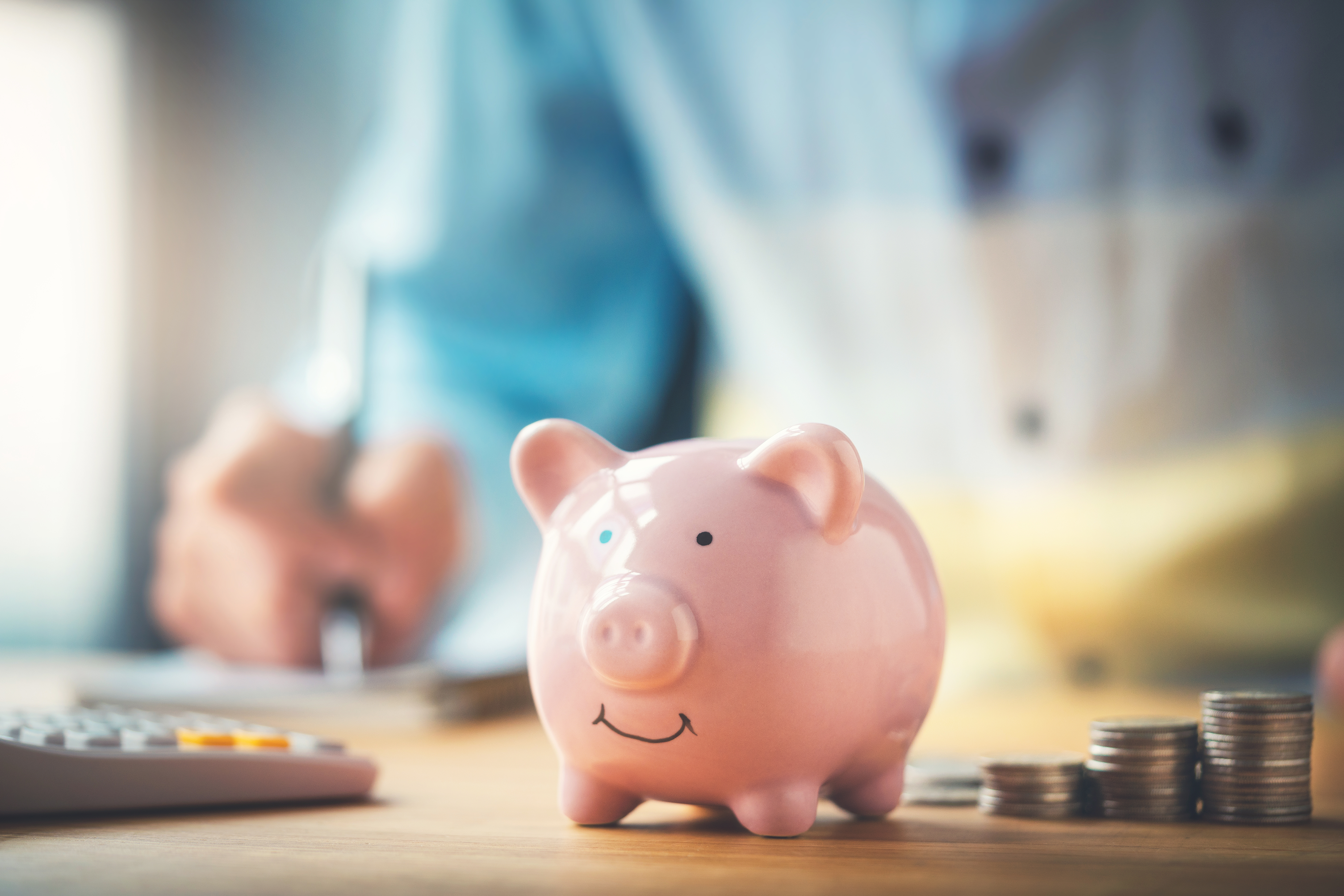 close up view of a piggy bank with a man working out numbers in the background